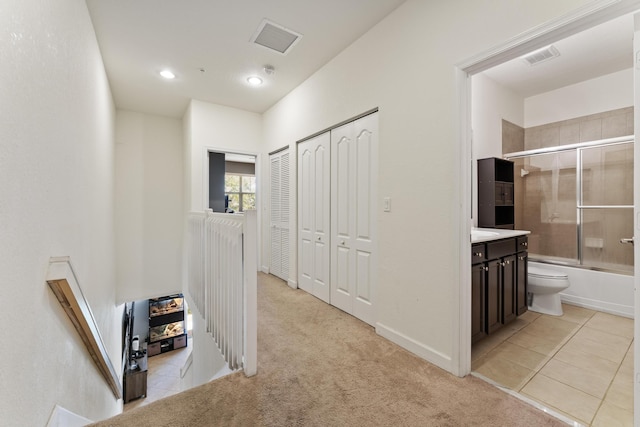 hall featuring light tile patterned floors, visible vents, and light carpet