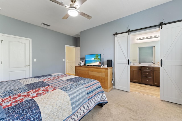 bedroom featuring visible vents, light colored carpet, a barn door, ensuite bath, and a ceiling fan