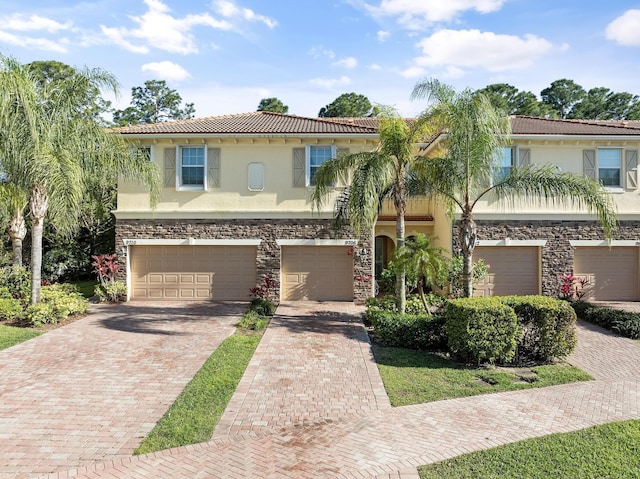 view of front of house featuring driveway, an attached garage, stucco siding, stone siding, and a tiled roof