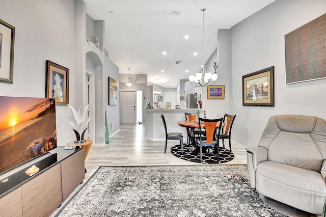 living room featuring visible vents, arched walkways, light wood-style floors, high vaulted ceiling, and a notable chandelier