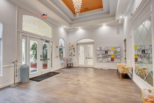 interior space featuring visible vents, a towering ceiling, wood finished floors, a tray ceiling, and french doors