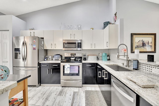 kitchen with lofted ceiling, a sink, appliances with stainless steel finishes, light wood-type flooring, and tasteful backsplash