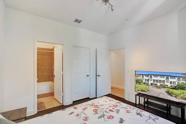 bedroom featuring visible vents, ensuite bathroom, baseboards, and wood finished floors