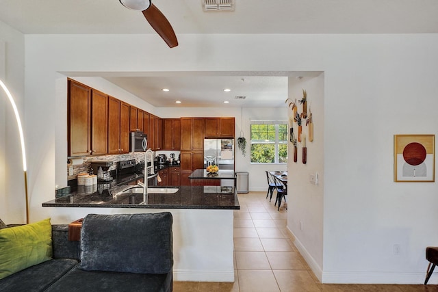 kitchen with light tile patterned floors, appliances with stainless steel finishes, a sink, dark stone countertops, and a peninsula