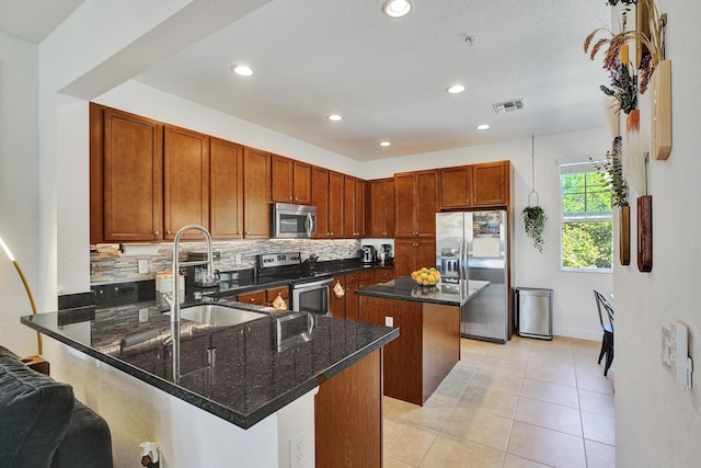 kitchen with a peninsula, a sink, visible vents, appliances with stainless steel finishes, and dark stone countertops