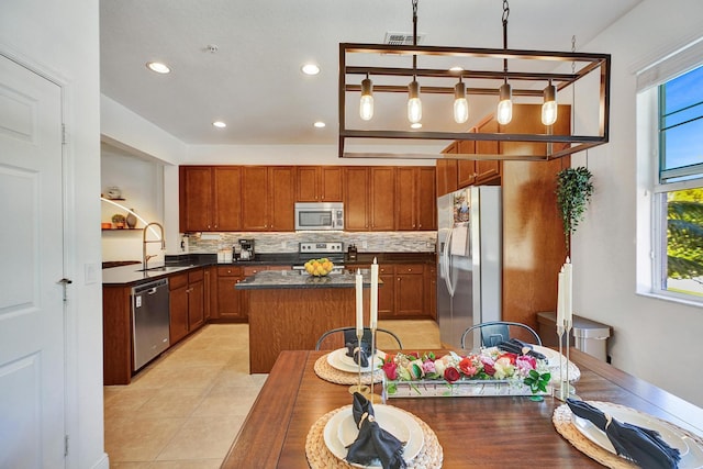 kitchen with appliances with stainless steel finishes, dark countertops, a kitchen island, and a healthy amount of sunlight