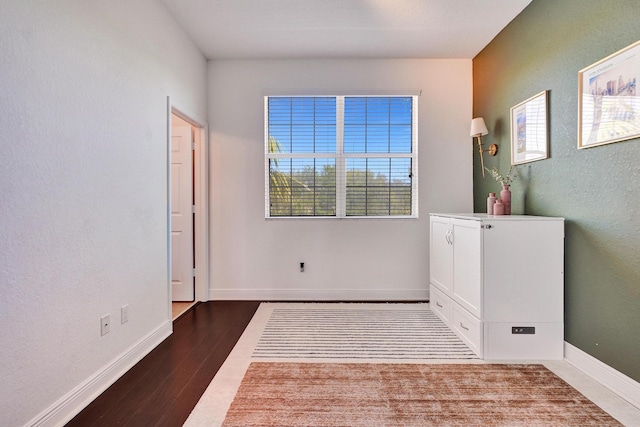 spare room featuring a textured wall, wood finished floors, and baseboards