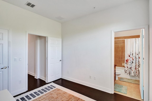 unfurnished bedroom featuring ensuite bathroom, dark wood finished floors, visible vents, and baseboards