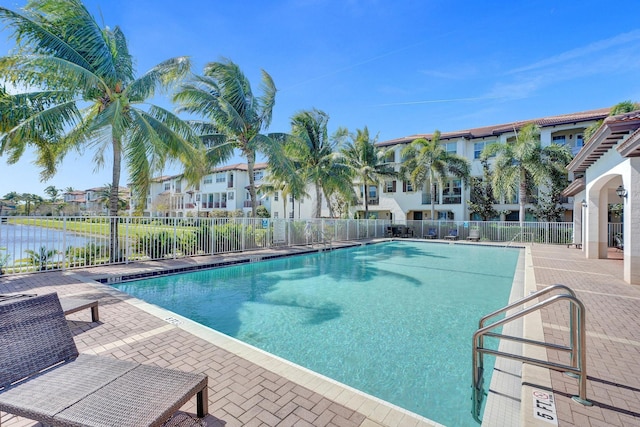 community pool with a residential view, a patio area, fence, and a water view