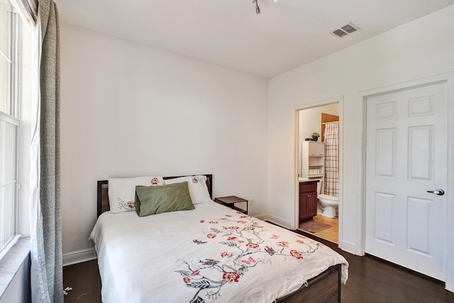 bedroom with connected bathroom, visible vents, dark wood finished floors, and baseboards