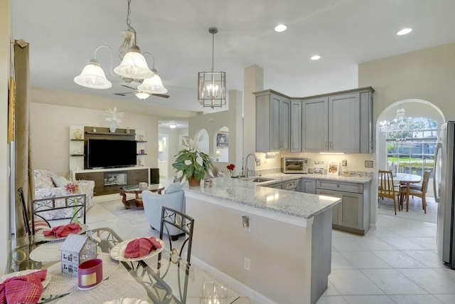 kitchen featuring arched walkways, freestanding refrigerator, light stone countertops, gray cabinets, and a sink