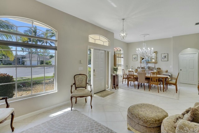 entrance foyer featuring arched walkways, light tile patterned floors, a notable chandelier, visible vents, and baseboards