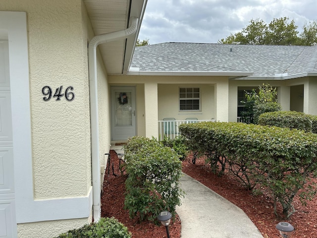 property entrance featuring stucco siding, cooling unit, and roof with shingles