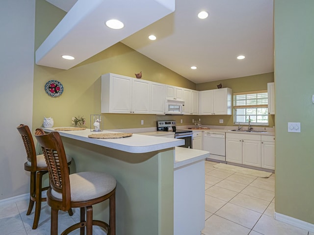 kitchen featuring a kitchen bar, a peninsula, light tile patterned flooring, white cabinets, and white appliances