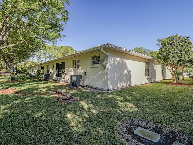 rear view of property with central air condition unit, a yard, and stucco siding