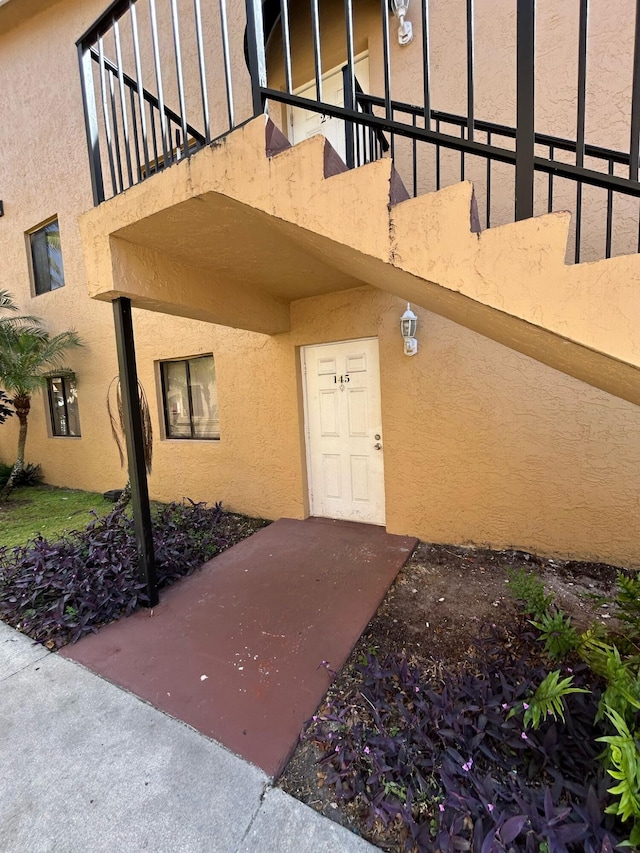 view of exterior entry with a balcony and stucco siding