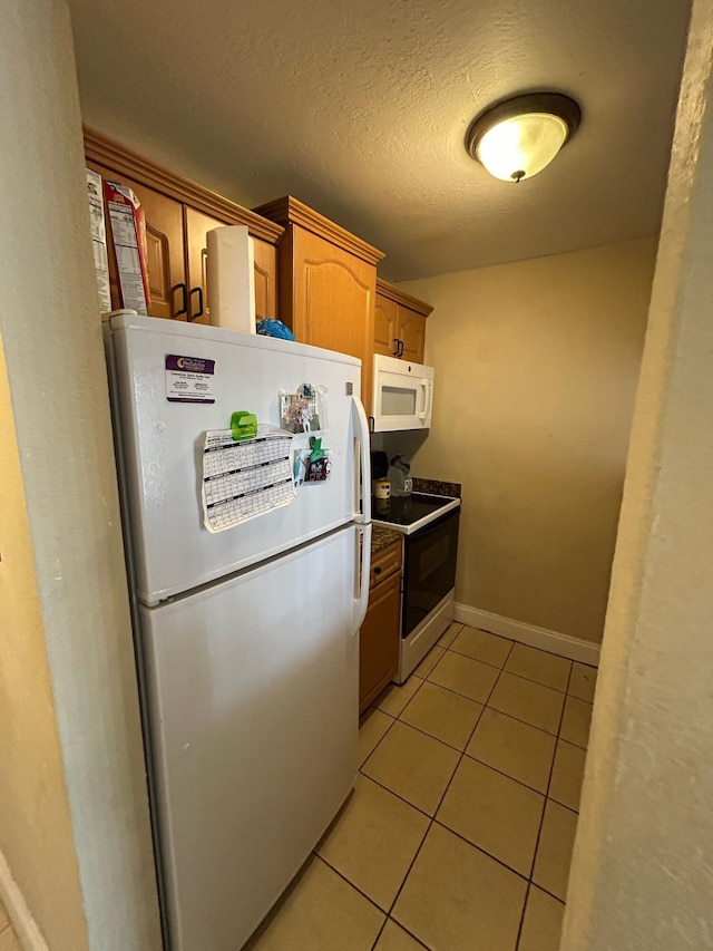 kitchen featuring light tile patterned floors, dark countertops, a textured ceiling, white appliances, and baseboards