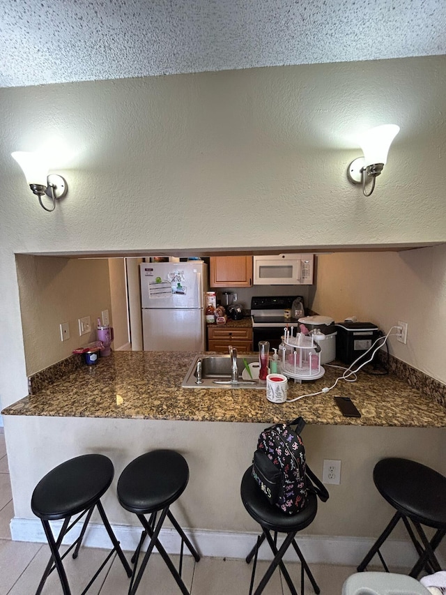 kitchen featuring dark countertops, white appliances, a peninsula, and a breakfast bar area