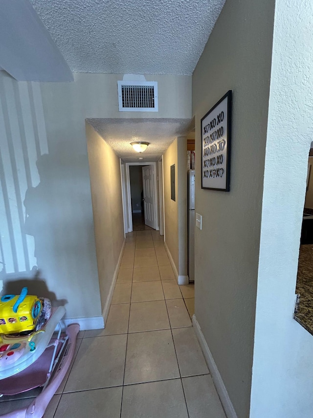 corridor featuring visible vents, a textured ceiling, baseboards, and light tile patterned floors