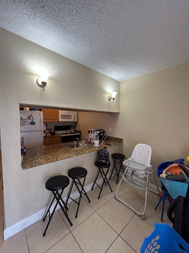 kitchen featuring white appliances, light tile patterned flooring, a sink, and a textured ceiling