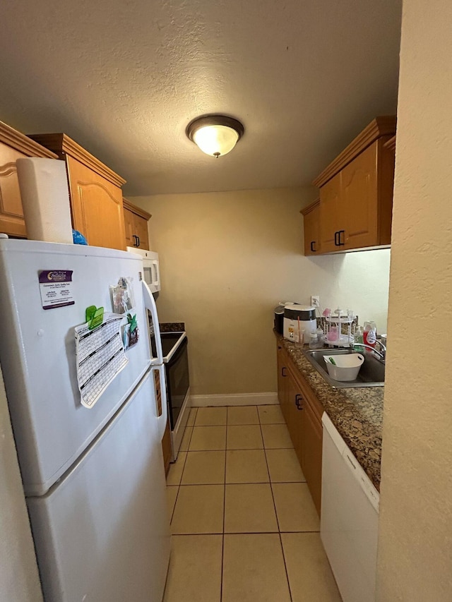 kitchen with white appliances, light tile patterned floors, baseboards, a textured ceiling, and a sink