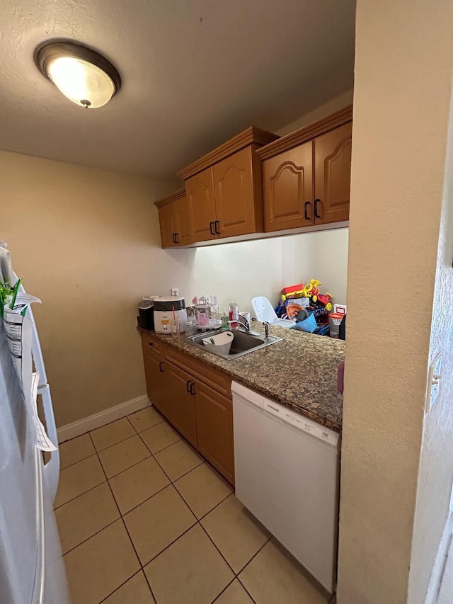 kitchen with light tile patterned floors, a sink, baseboards, dishwasher, and dark stone countertops