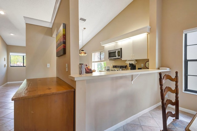 kitchen with light tile patterned floors, baseboards, stainless steel microwave, vaulted ceiling, and light countertops