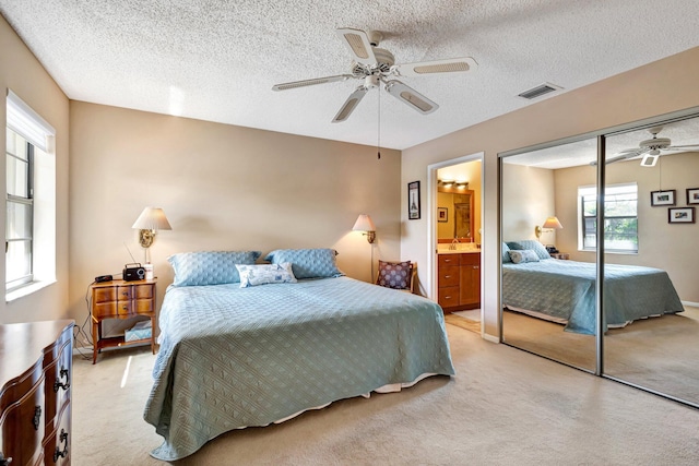 bedroom with ceiling fan, a textured ceiling, ensuite bathroom, light carpet, and visible vents