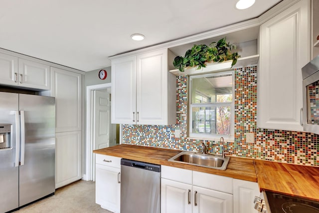 kitchen with stainless steel appliances, butcher block counters, a sink, and white cabinetry