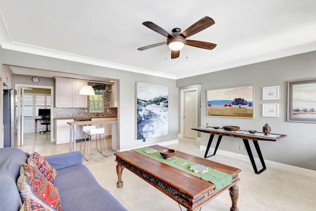 living area with ceiling fan, ornamental molding, and baseboards