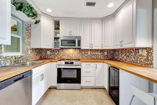 kitchen featuring beverage cooler, appliances with stainless steel finishes, wooden counters, and backsplash