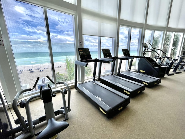 exercise room with a water view, floor to ceiling windows, a beach view, and a wealth of natural light