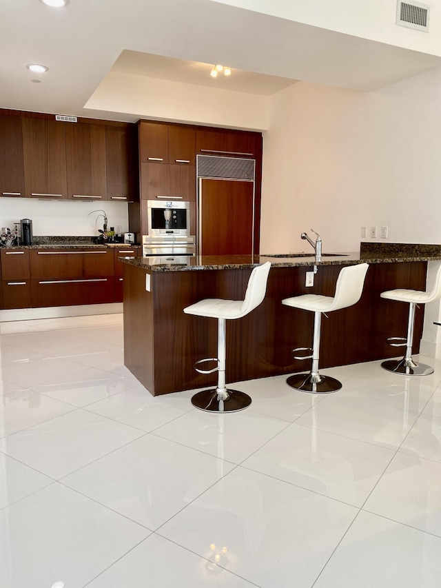 kitchen with modern cabinets, visible vents, a kitchen bar, and paneled built in refrigerator