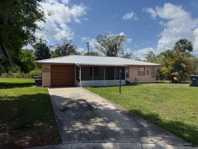 ranch-style home featuring a garage, driveway, a front lawn, and metal roof