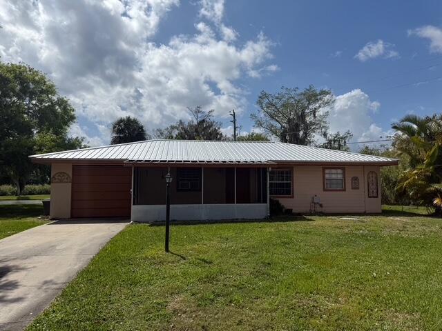 view of front of home with a garage, concrete driveway, metal roof, and a front yard