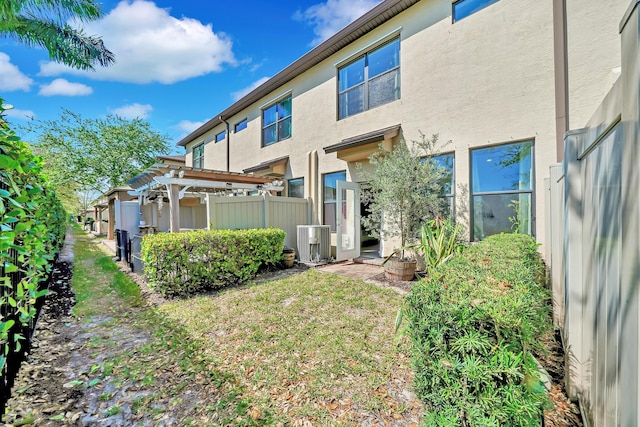 back of property featuring stucco siding, fence, central AC, and a pergola