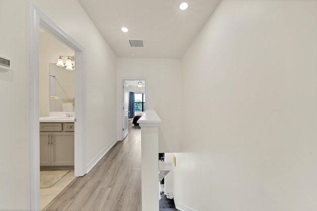 corridor with visible vents, baseboards, recessed lighting, light wood-style flooring, and a sink