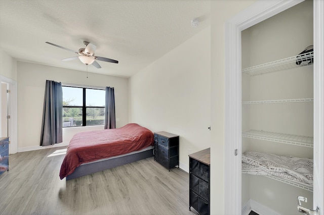 bedroom with light wood-type flooring, baseboards, a textured ceiling, and ceiling fan