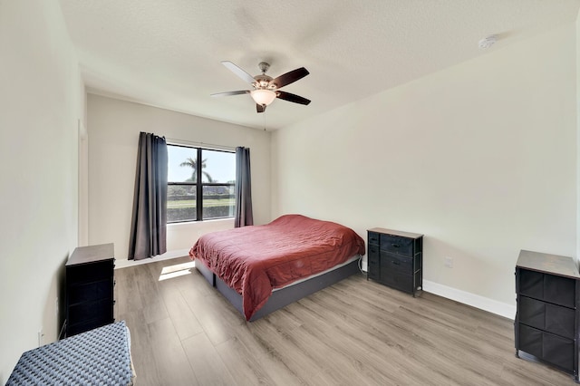 bedroom featuring ceiling fan, light wood-style floors, baseboards, and a textured ceiling