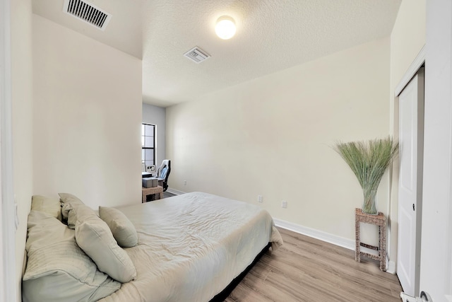 bedroom with visible vents, a textured ceiling, baseboards, and wood finished floors