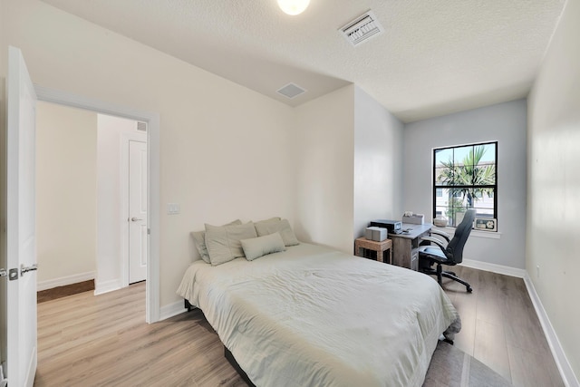 bedroom with a textured ceiling, baseboards, visible vents, and light wood-type flooring