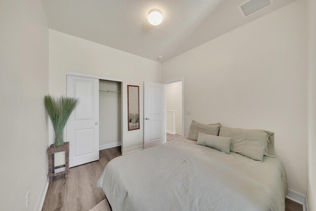 bedroom featuring visible vents, light wood-style flooring, a textured ceiling, a closet, and baseboards