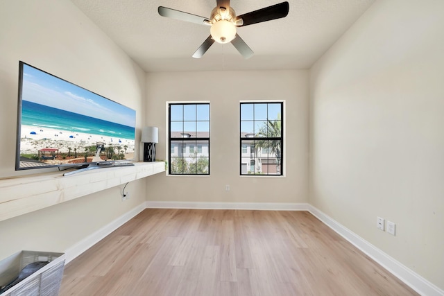 unfurnished room featuring light wood finished floors, ceiling fan, a textured ceiling, and baseboards