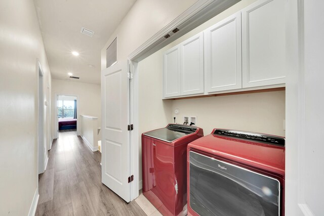 laundry room featuring visible vents, light wood-type flooring, washer and clothes dryer, cabinet space, and baseboards