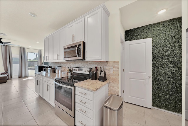 kitchen featuring light stone counters, white cabinetry, stainless steel appliances, light tile patterned floors, and decorative backsplash