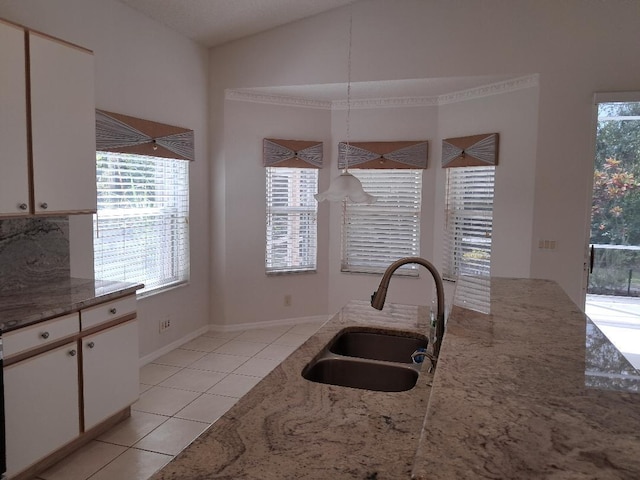 kitchen featuring light tile patterned floors, a sink, a wealth of natural light, and light stone countertops