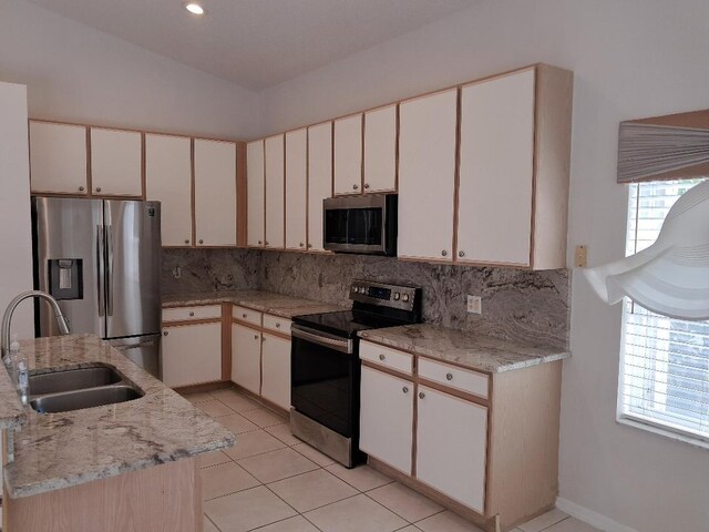 kitchen with light tile patterned floors, lofted ceiling, appliances with stainless steel finishes, a sink, and backsplash