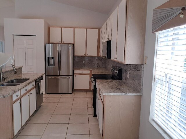 kitchen featuring light tile patterned floors, a sink, vaulted ceiling, backsplash, and black appliances