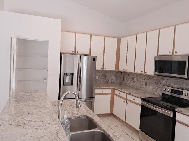 kitchen featuring tasteful backsplash, stainless steel appliances, white cabinetry, a sink, and light tile patterned flooring