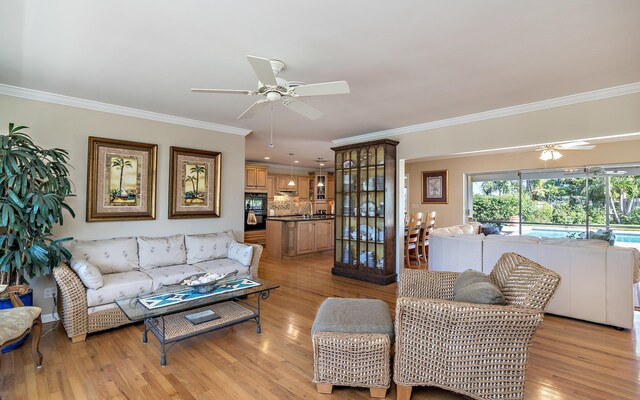 living area with light wood-style floors, ornamental molding, and a ceiling fan